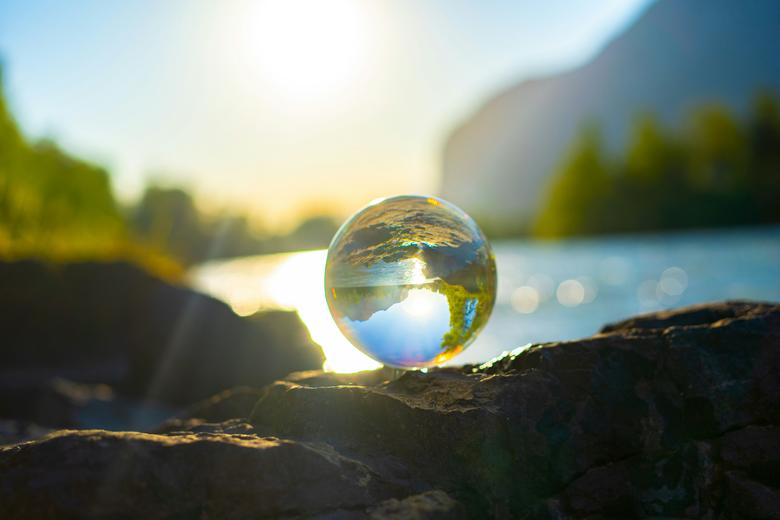 A glass ball reflecting water, trees and rocks, similar to a globe.