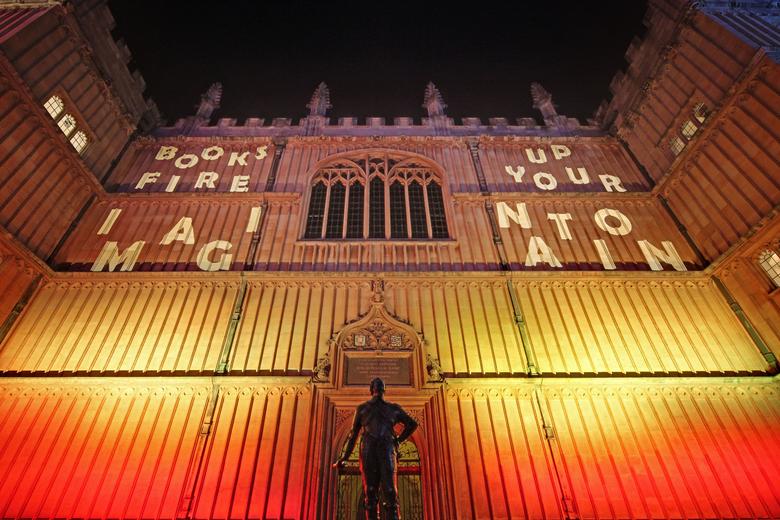 Photo of the side of the old bodleian library with fire colours projected onto it and the words 'Books fire up your imagination'