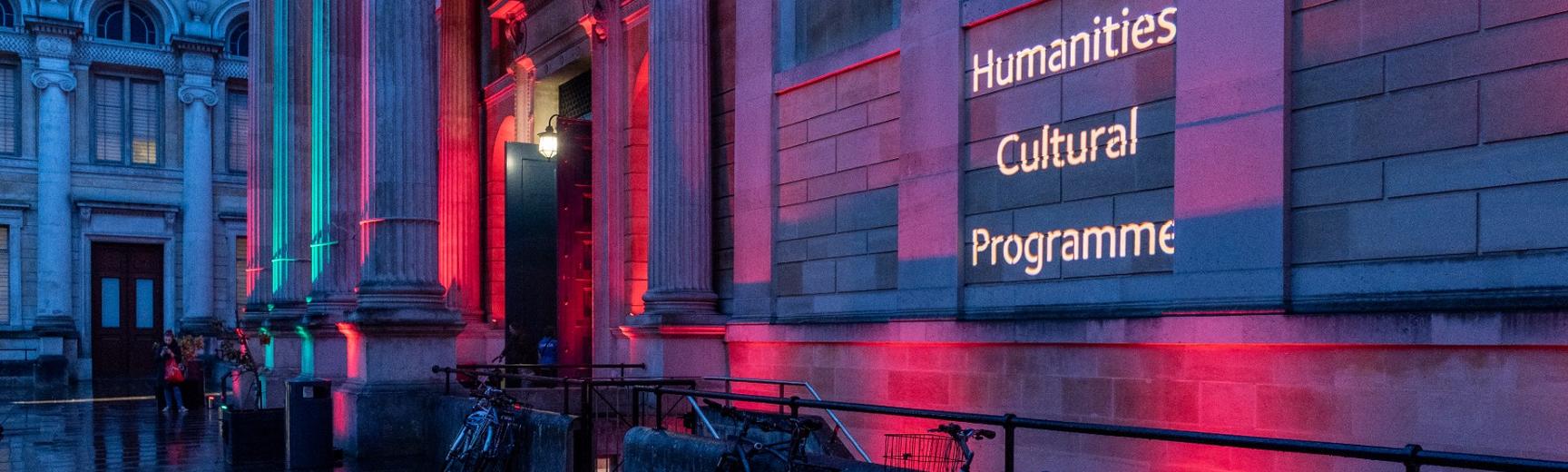 Museum front lit in blue and pink lights with 'Humanities Cultural Programme' projected in white letters 