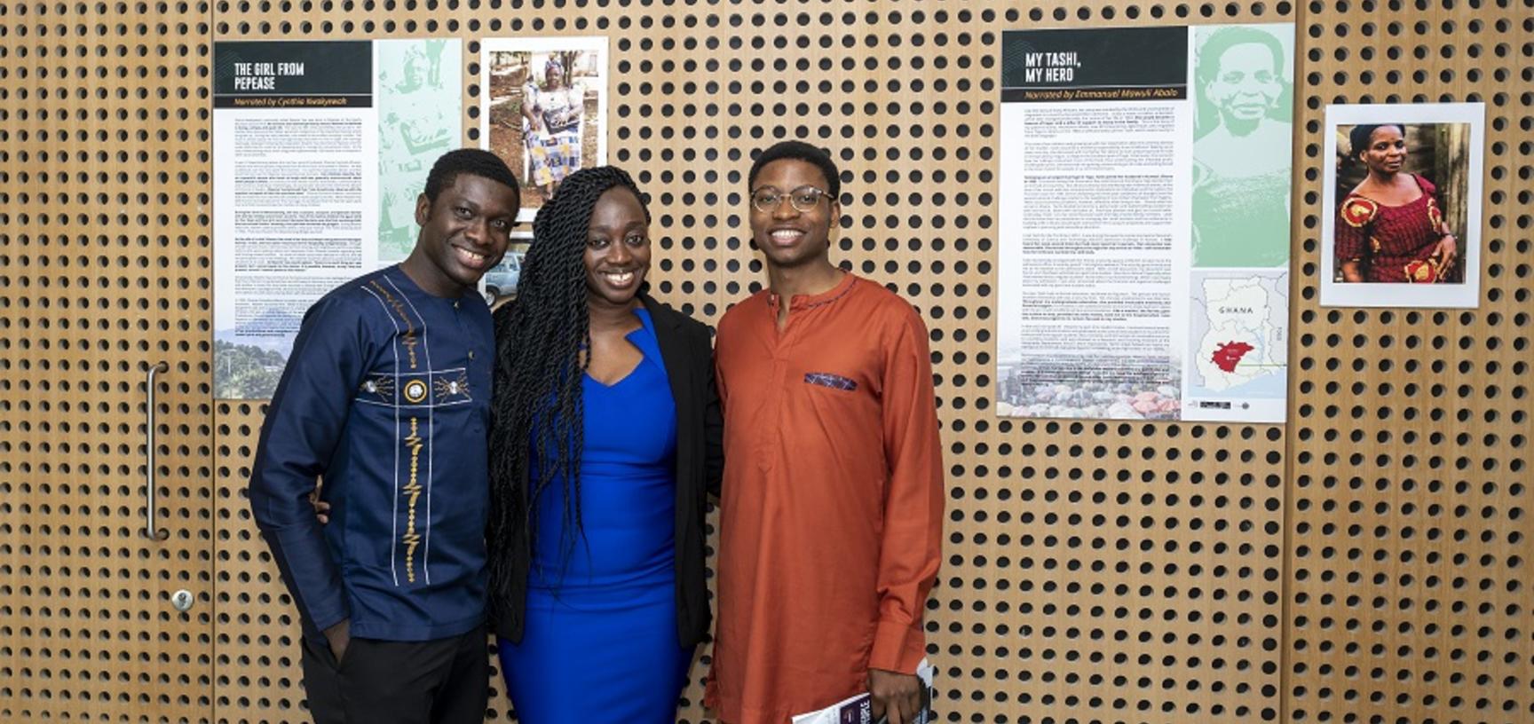 3 people smile at the camera in front of their poster exhibit