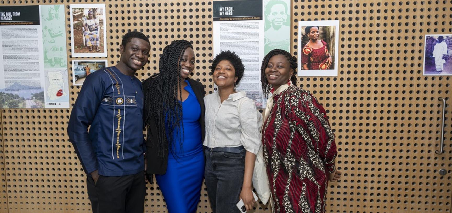 4 people smile at the camera in front of the poster exhibit