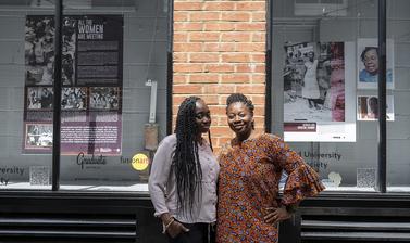 two women smiling in front of window display