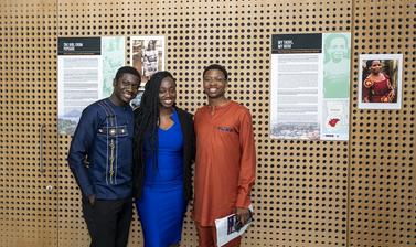 3 people smile at the camera in front of their poster exhibit
