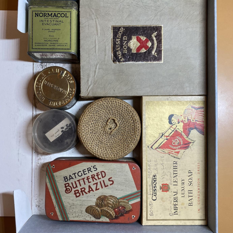 Old-fashioned metal tins and cardboard boxes originally containing nuts, soap, and medicine, in an archival box