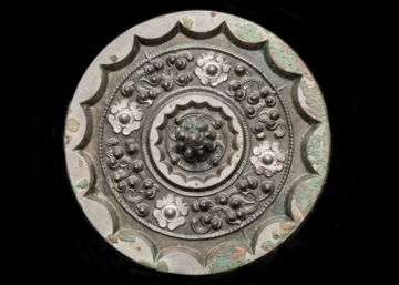 Back view of a bronze mirror decorated with star and cloud pattern. The knob at the centre of the mirror is cast as a mountain, surrounded by four small bosses and an abbreviated cloud design. The thickened rim of the mirror is cast with sixteen arcs. 