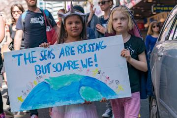 children hold signs for climate crisis awareness which reads 'the seas are rising but so are we!'