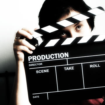 A woman holding an open clapperboard. You can see her eyes through the opening. 