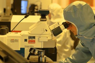 Person in protective suit looking through a high-tech microscope