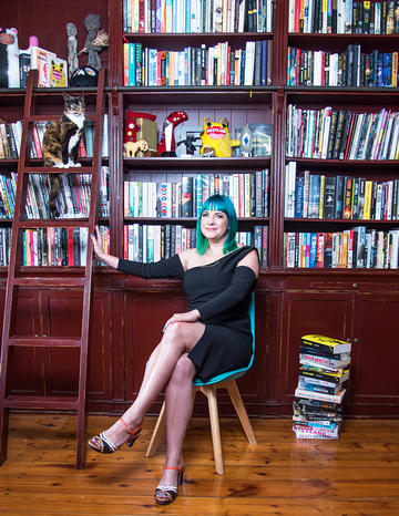 Lauren Beukes sitting on chair in front of wooden bookshelves
