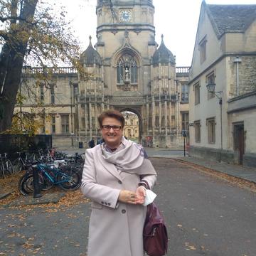 woman in tan trench coat standing in front of a college at Oxford