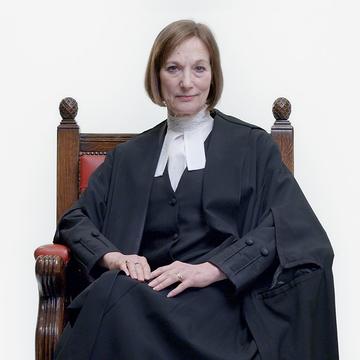 Carey Young, wearing a judge's gown, looks into the camera