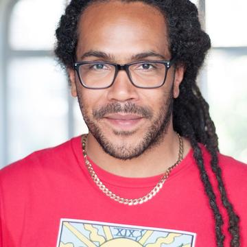 Rawz, a man with long dreadlocks and glasses, smiles at the camera.