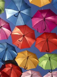 Image of yellow, orange, green, blue, pink, and purple umbrellas in the air against the blue sky background