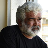 mheadshot of man with white hair and beard, wearing black top, looking out to the right