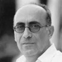 black and white photo of man with glasses sitting side on to camera wearing white shirt