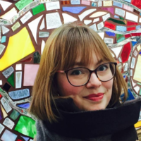 Emma Parker smiling in front of colorful mosaic wall art