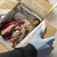 Image depicts the unpacking of a 18th century doll's house doll wearing a lace embroidered red gown (Nostell Priory, West Yorkshire).