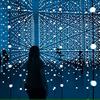Silhouette of a figure in a dark blue, mirrored room with strings of lights