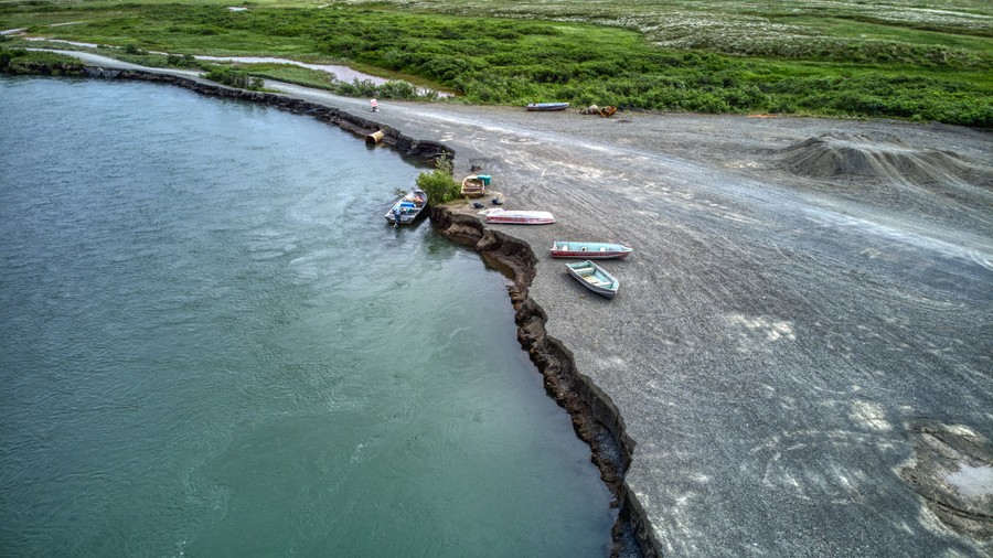Aerial view of a gravel bar eroding into the river, with four boats at the erosion face.